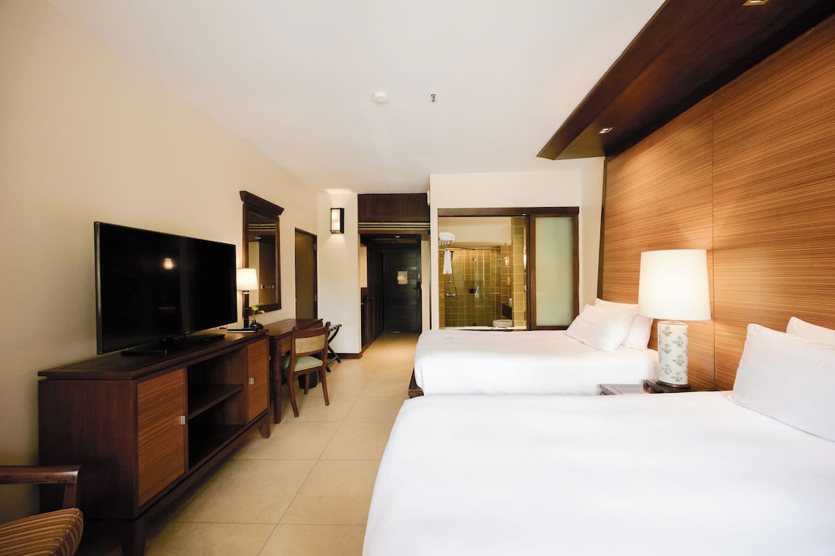 A hotel room with a TV, two beds, a desk, and a chair.