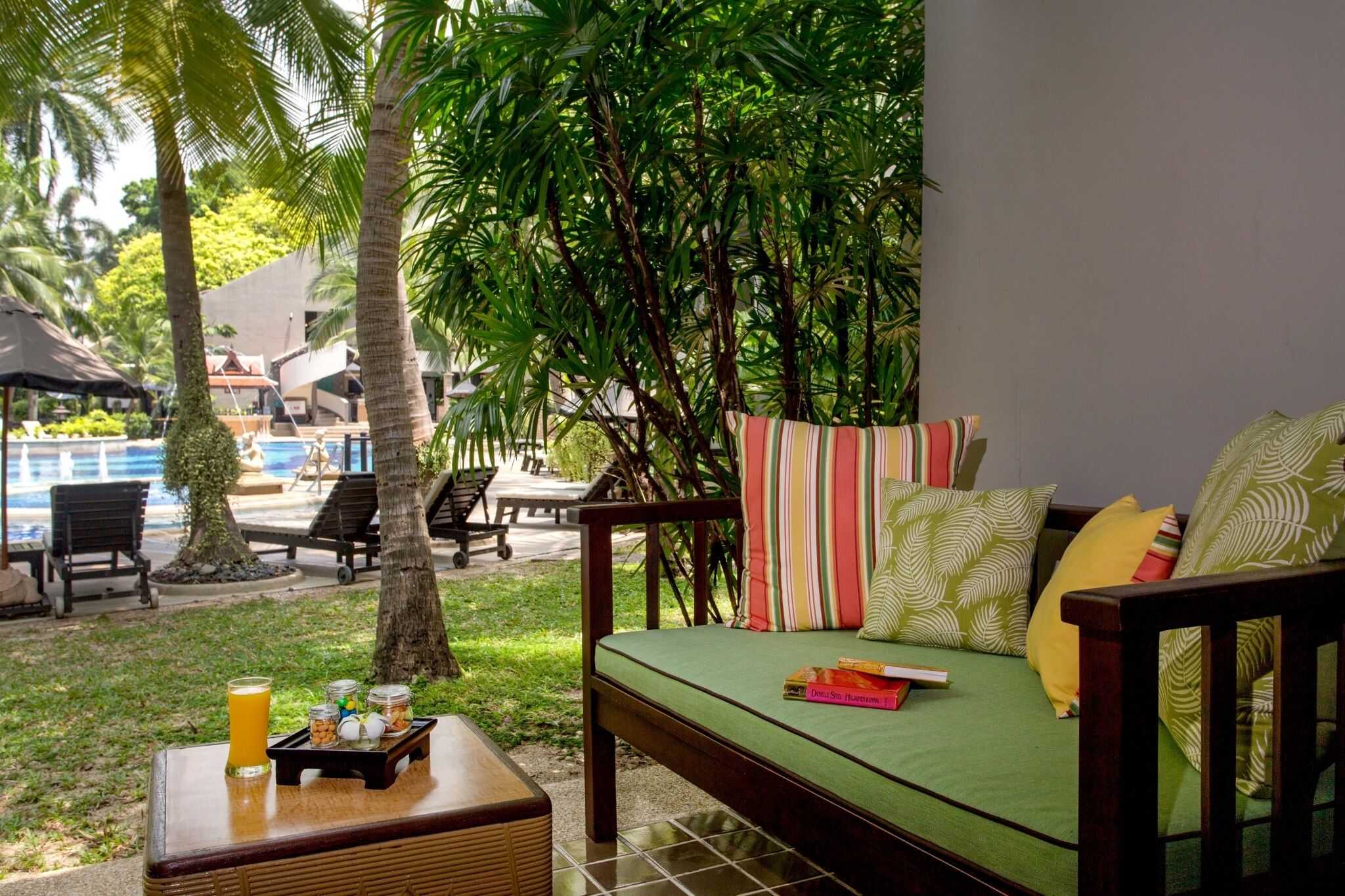 A cozy outdoor seating area with a green sofa, striped pillows, and a small table with a glass of orange juice and jars.