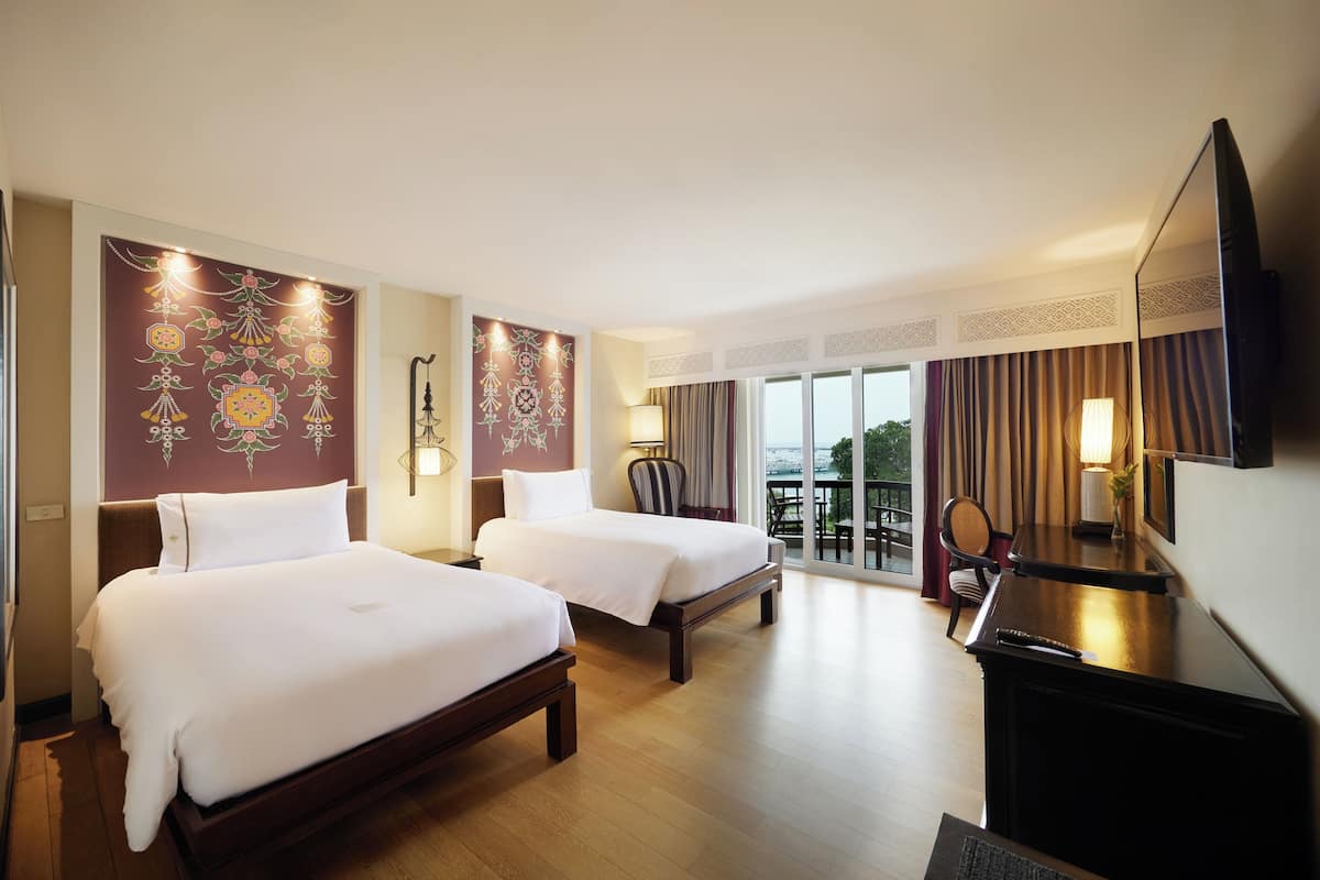 A hotel room with two beds, a desk, a chair, a TV, and a balcony with a view.