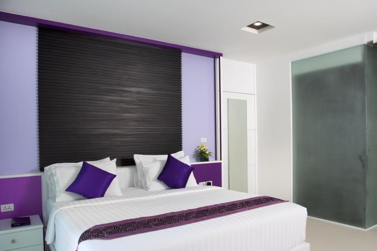 A modern bedroom with a large bed, purple accent walls, a dark headboard, and a large mirror.