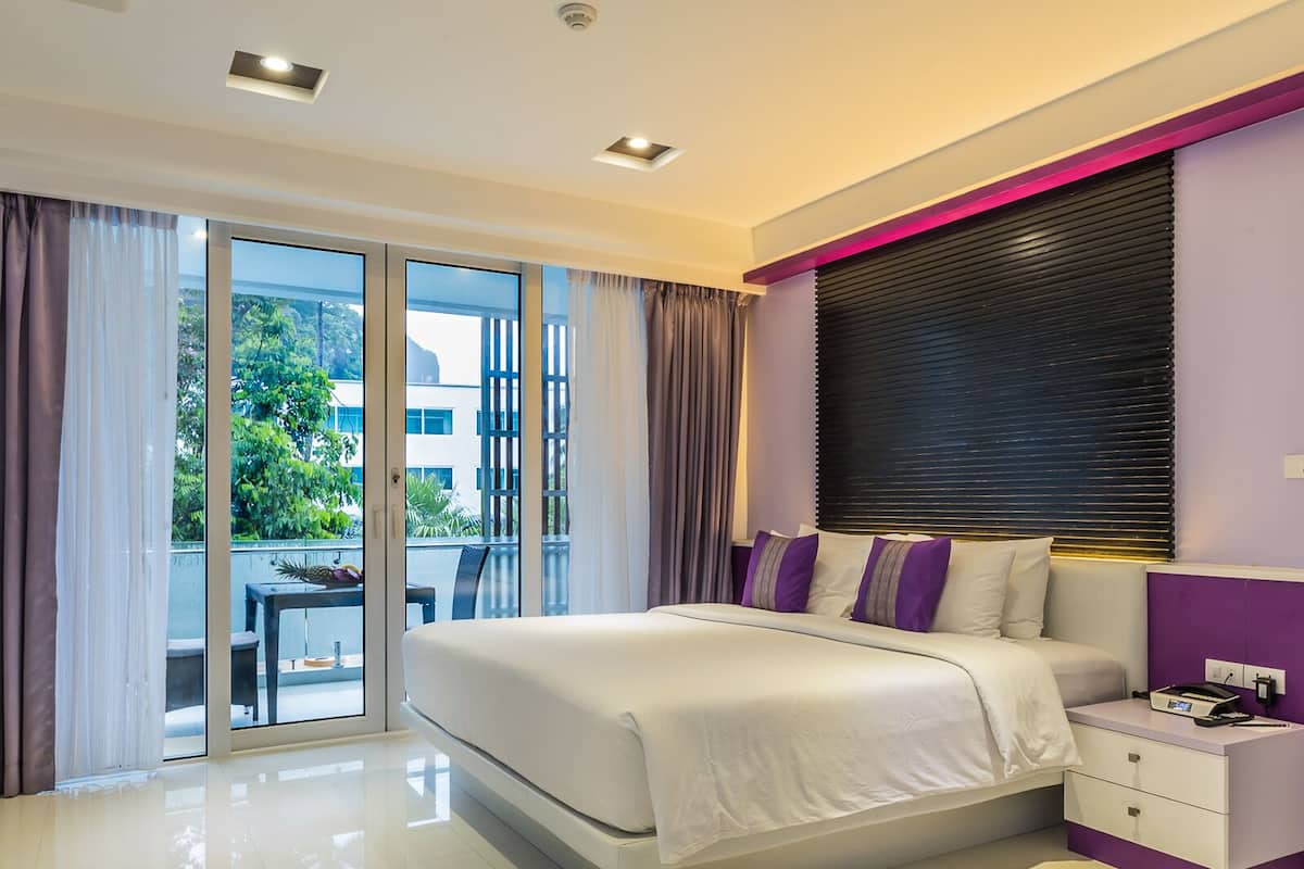 Habitación de hotel moderna con una cama grande, una mesita de noche y vistas al exterior a través de un ventanal corredero.
