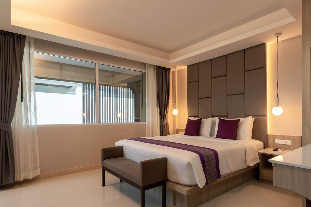 Una habitación de hotel moderna con una cama grande, una mesita de noche, una silla y un ventanal con cortinas.