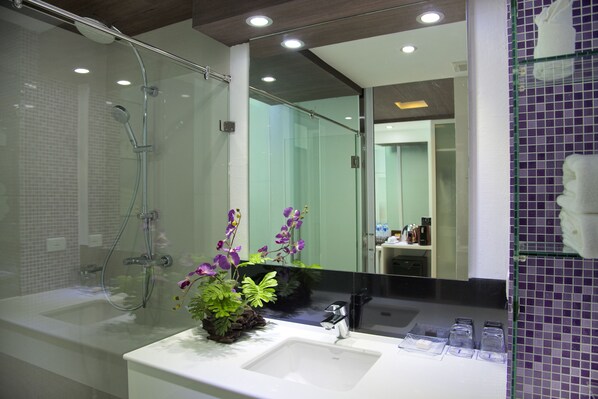 A modern bathroom with a glass shower enclosure, a white sink with a plant, and a large mirror reflecting the room.