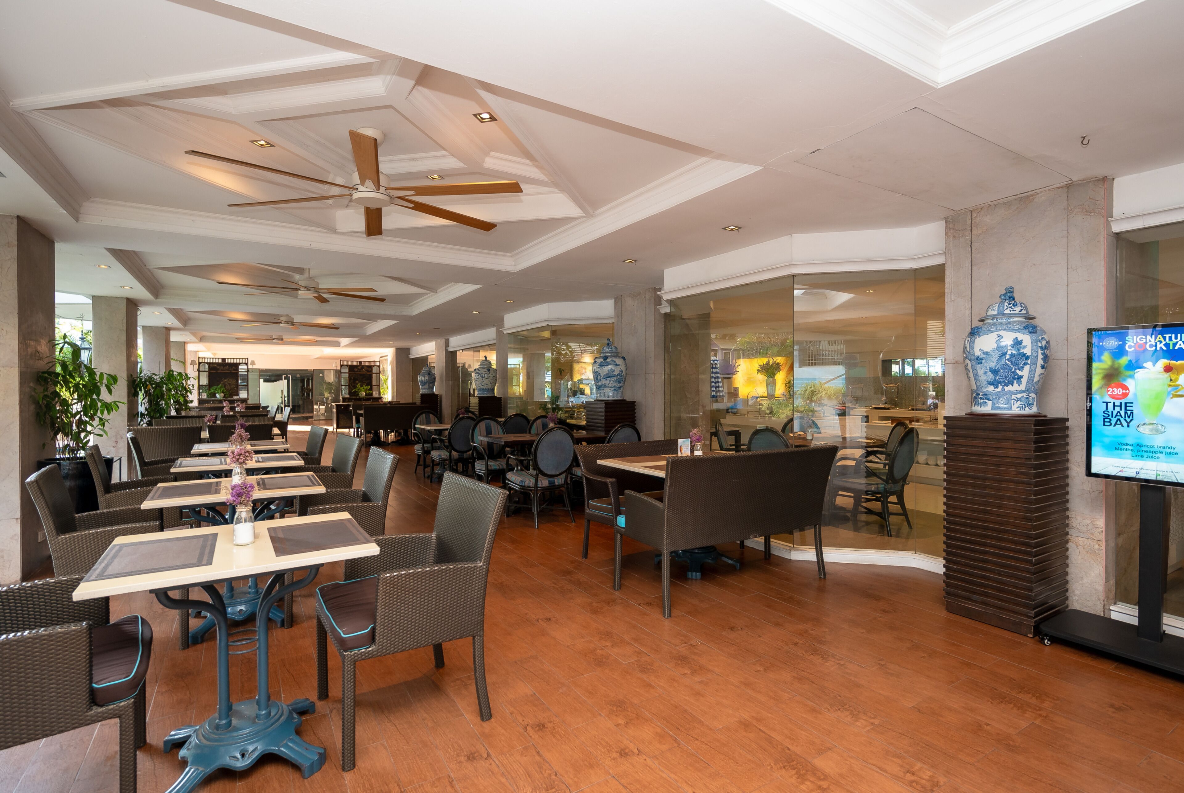 A spacious indoor dining area with high ceilings, ceiling fans, and a large TV screen.