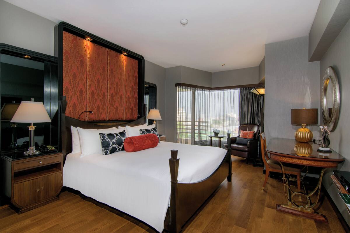 A hotel room with a large bed, two bedside tables with lamps, a chair, a desk with a lamp, and a large mirror on the wall.