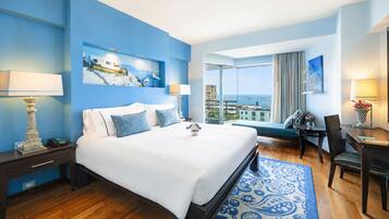 Habitación de hotel con una cama grande, un escritorio, una silla, vista al mar y un cuadro en la pared.