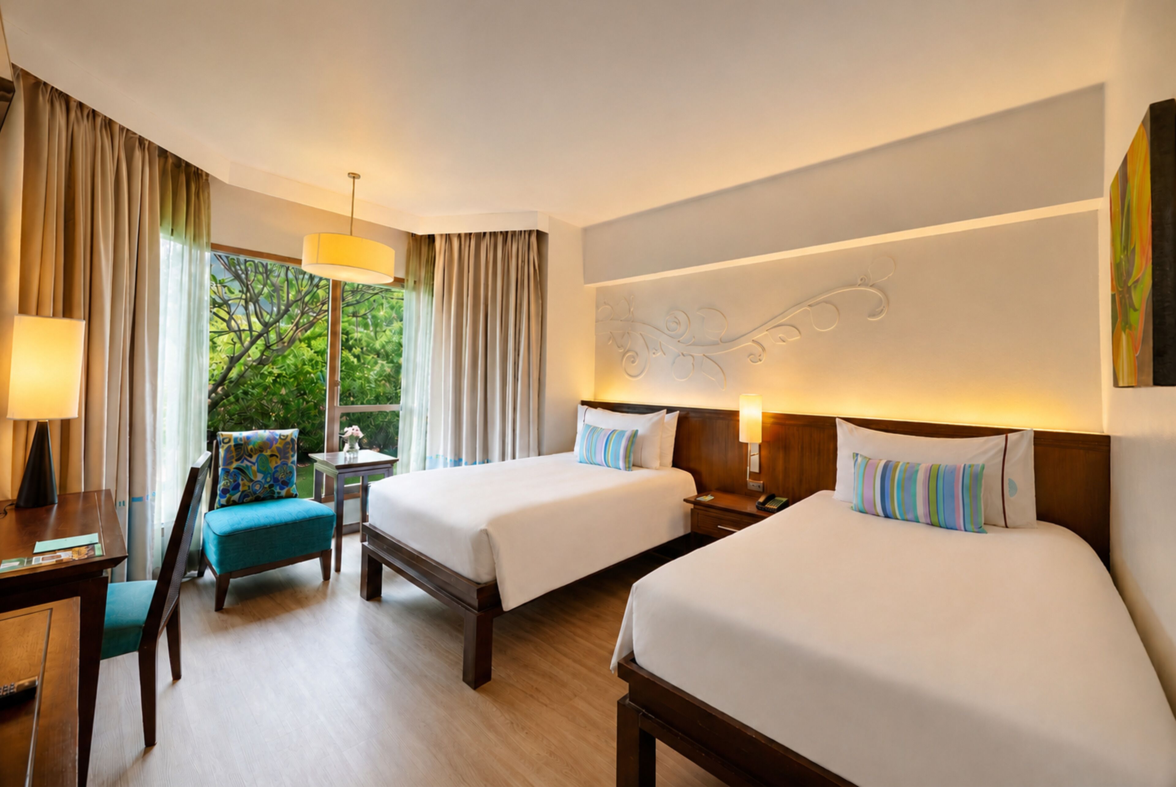 A hotel room with two beds, a desk, a chair, a lamp, and a window with curtains.