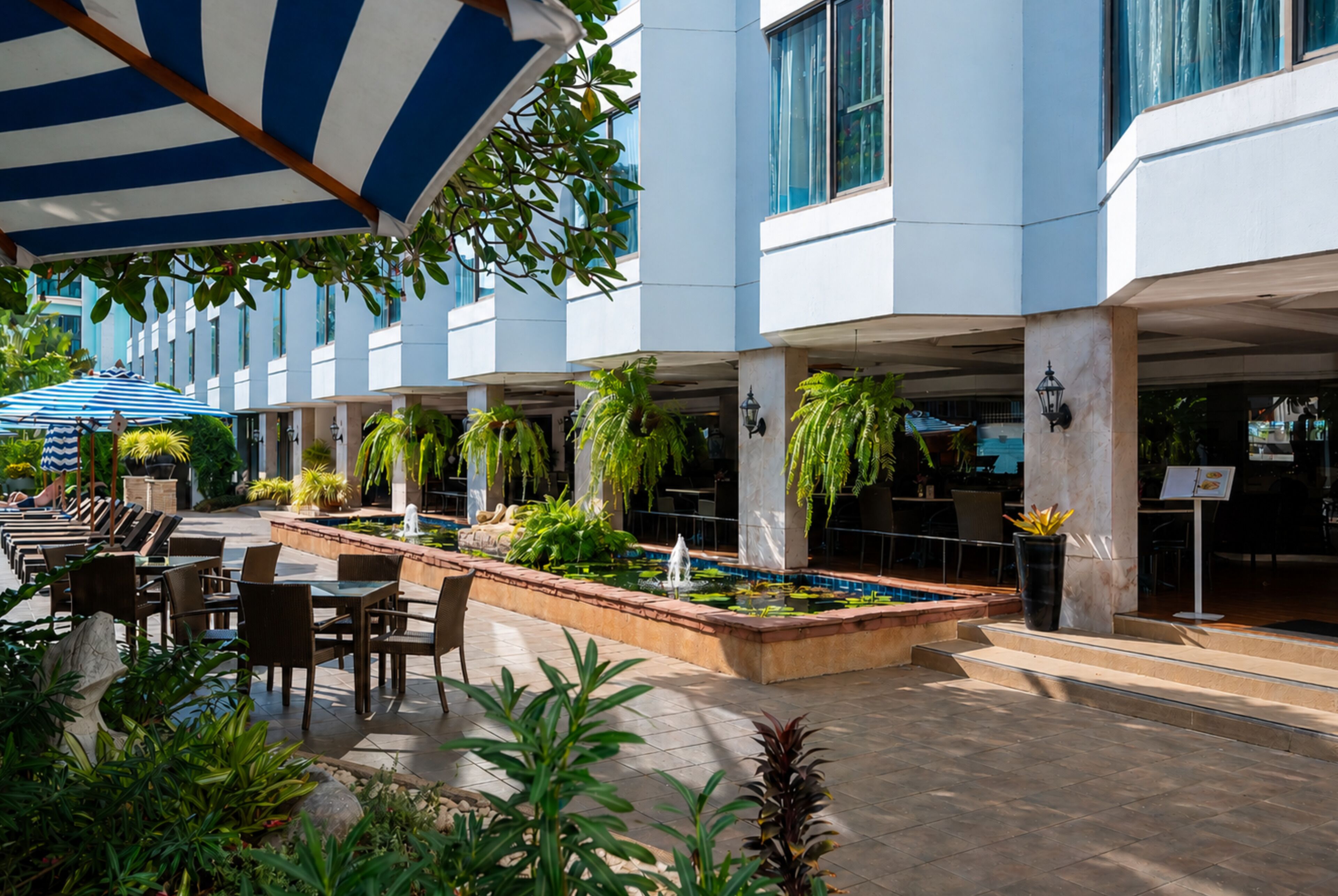 A hotel lobby with outdoor seating, a water feature, and lush greenery.