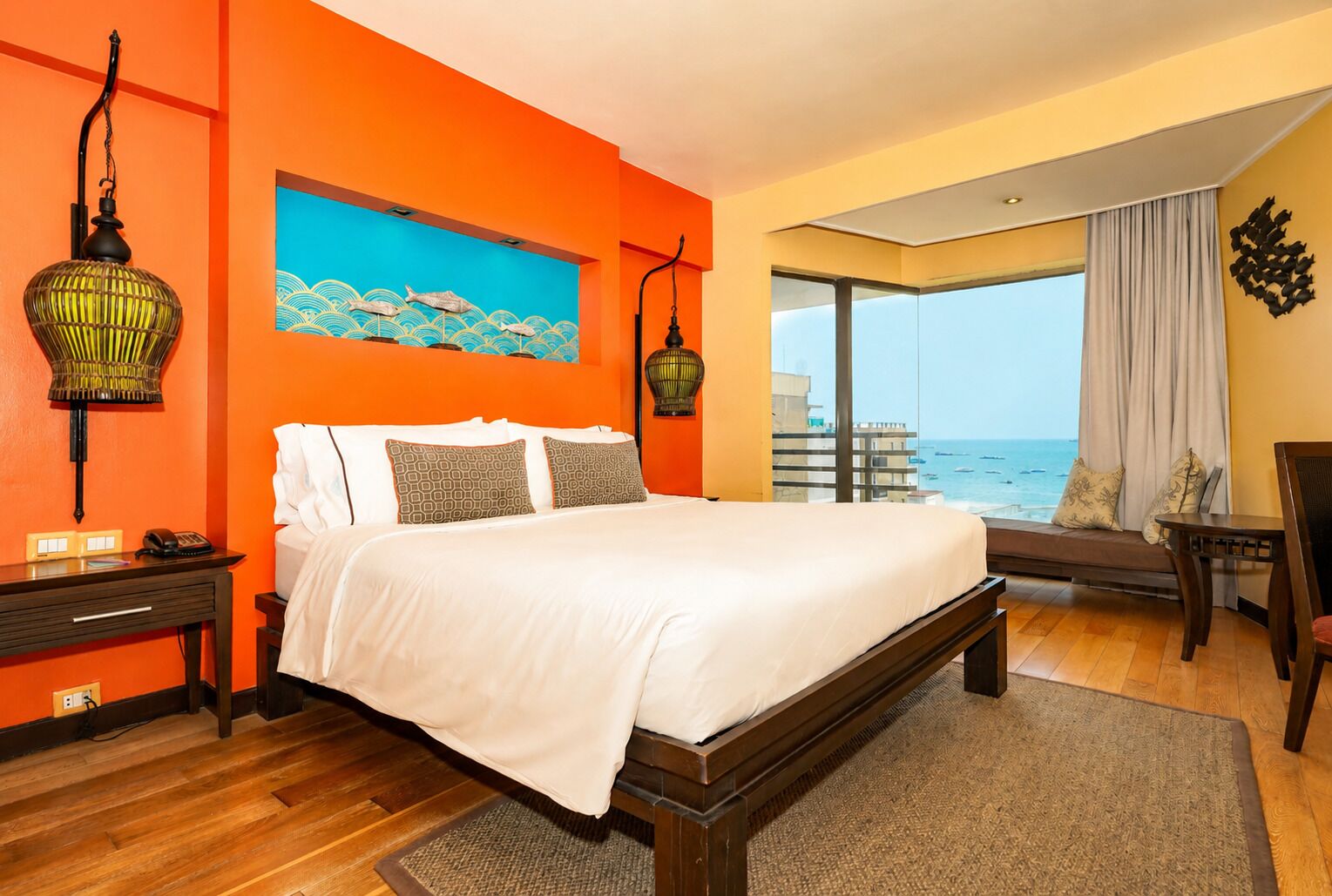 A bedroom with a bed, a nightstand, a lamp, a painting, a window with a view of the sea, and a balcony.