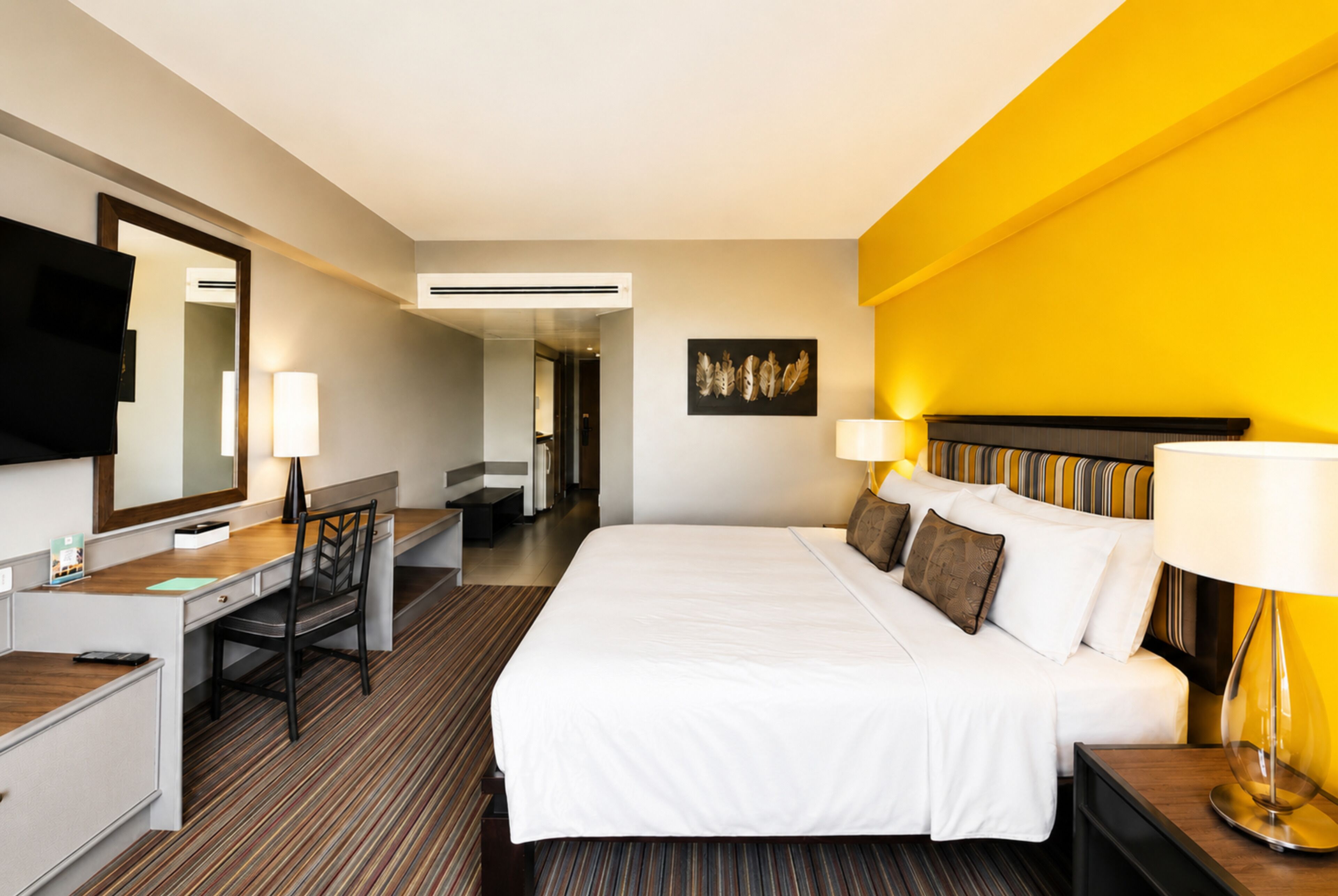 A hotel room with a bed, a desk, a chair, a television, and a wall-mounted artwork.