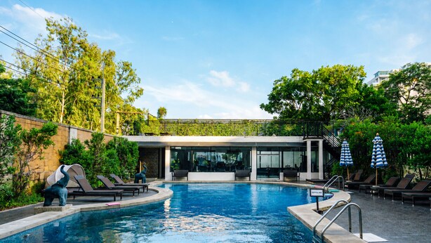 A swimming pool with lounge chairs and umbrellas, surrounded by greenery and a building with large windows. - The Bayview Hotel Pattaya (Pattaya)
