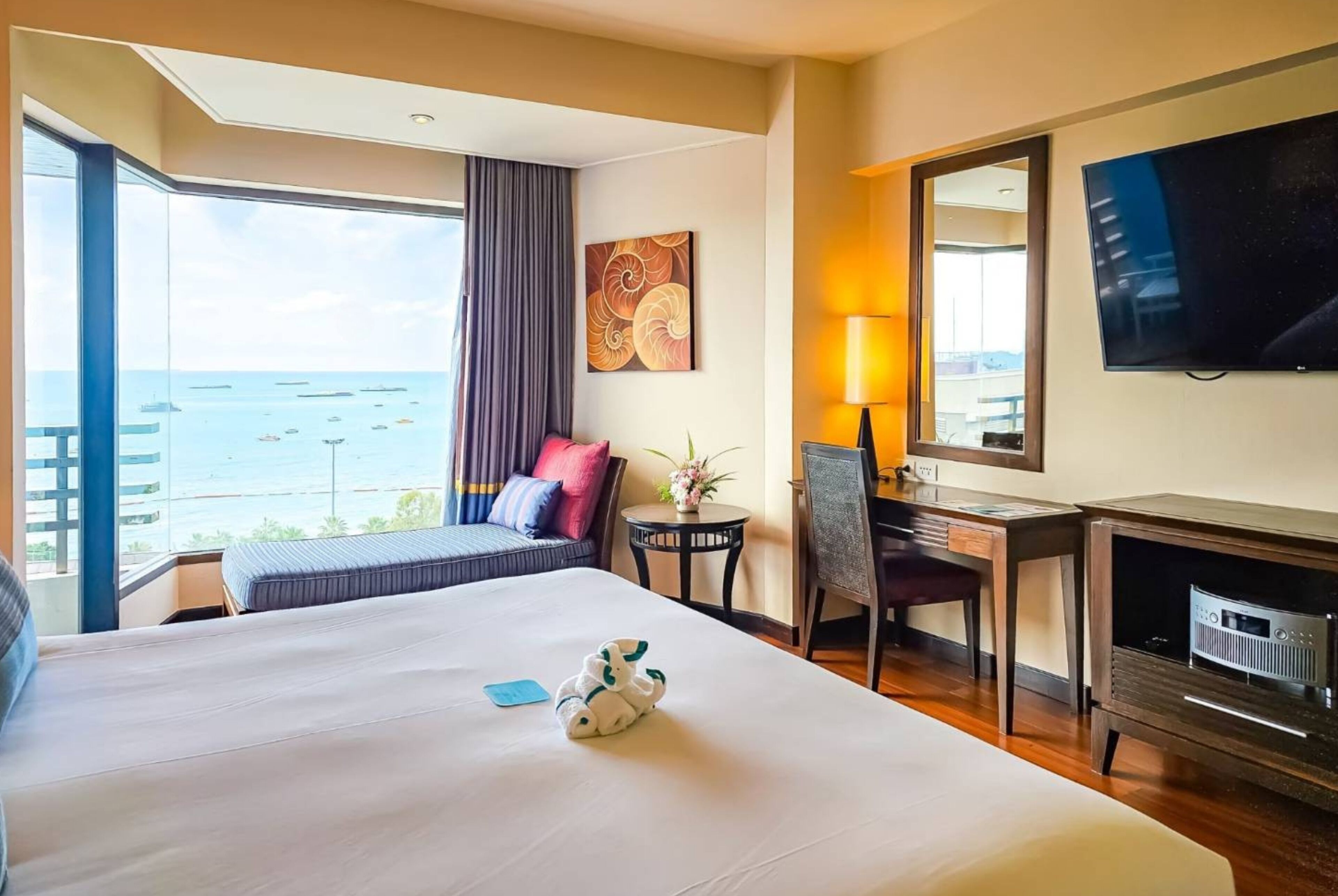 Habitación de hotel con cama, escritorio, silla, televisor y vista al mar.