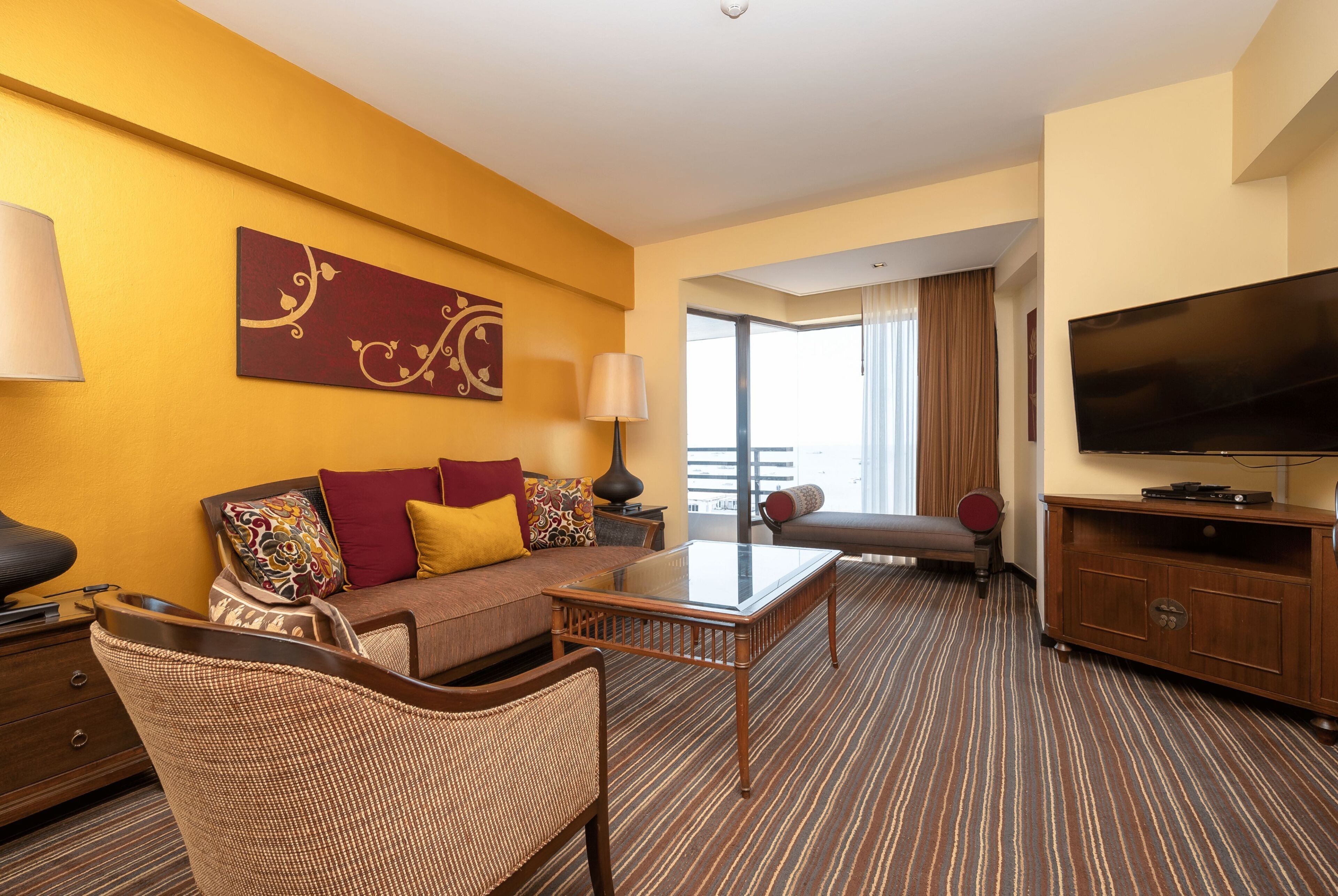 A hotel room with a sofa, armchair, television, and a large window.