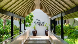 A covered walkway with a sign reading 'The Garden Wing,' surrounded by lush greenery and large potted plants. - The Bayview Hotel Pattaya (Pattaya)