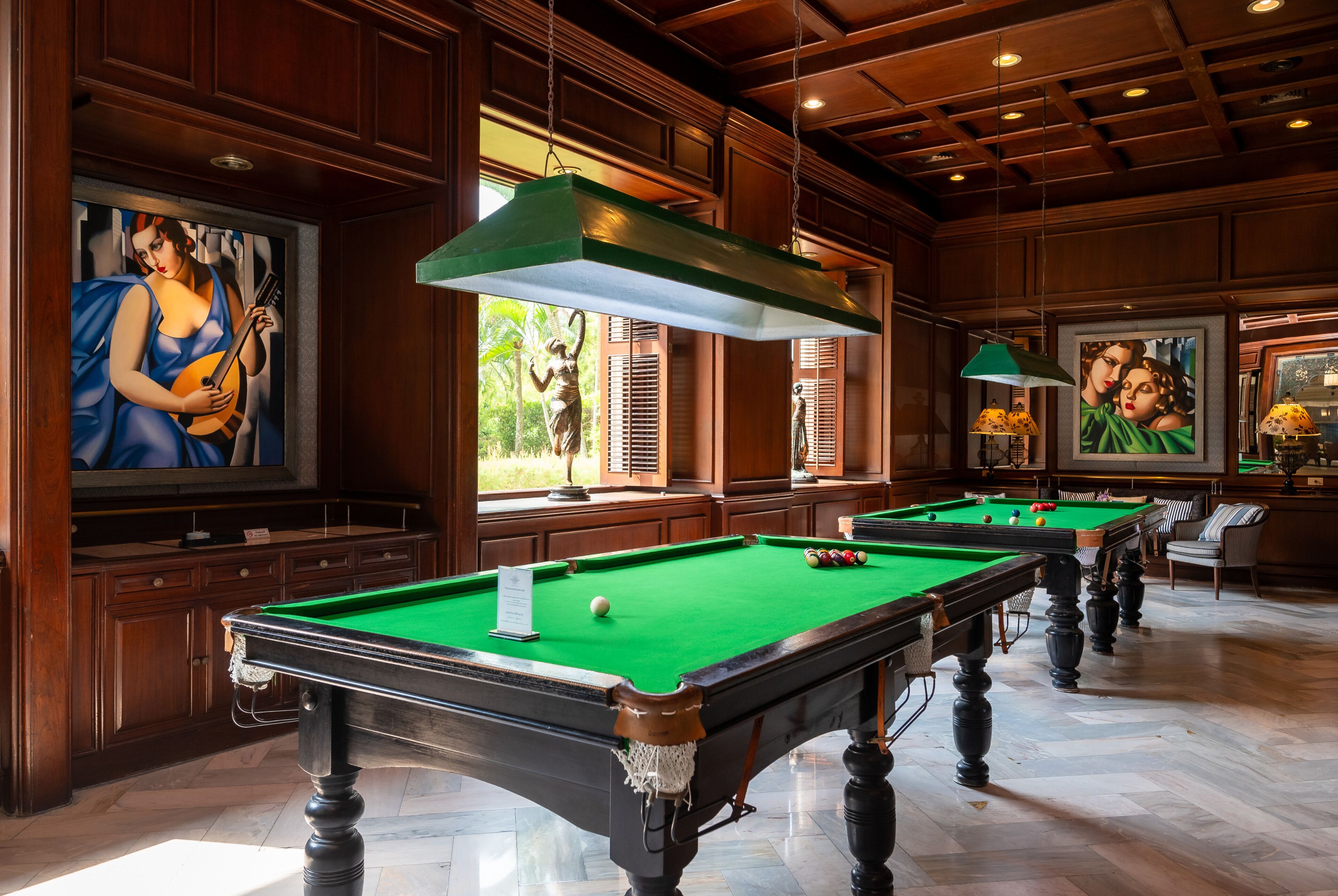 Une salle de billard dotée de plusieurs tables de billard, de boiseries et d’œuvres d’art accrochées aux murs.