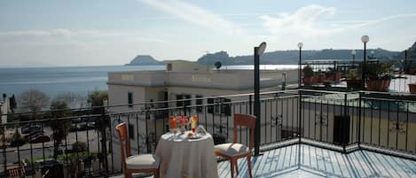 En terrasse med et bord dækket til to, med udsigt over vand og fjerne omgivelser.