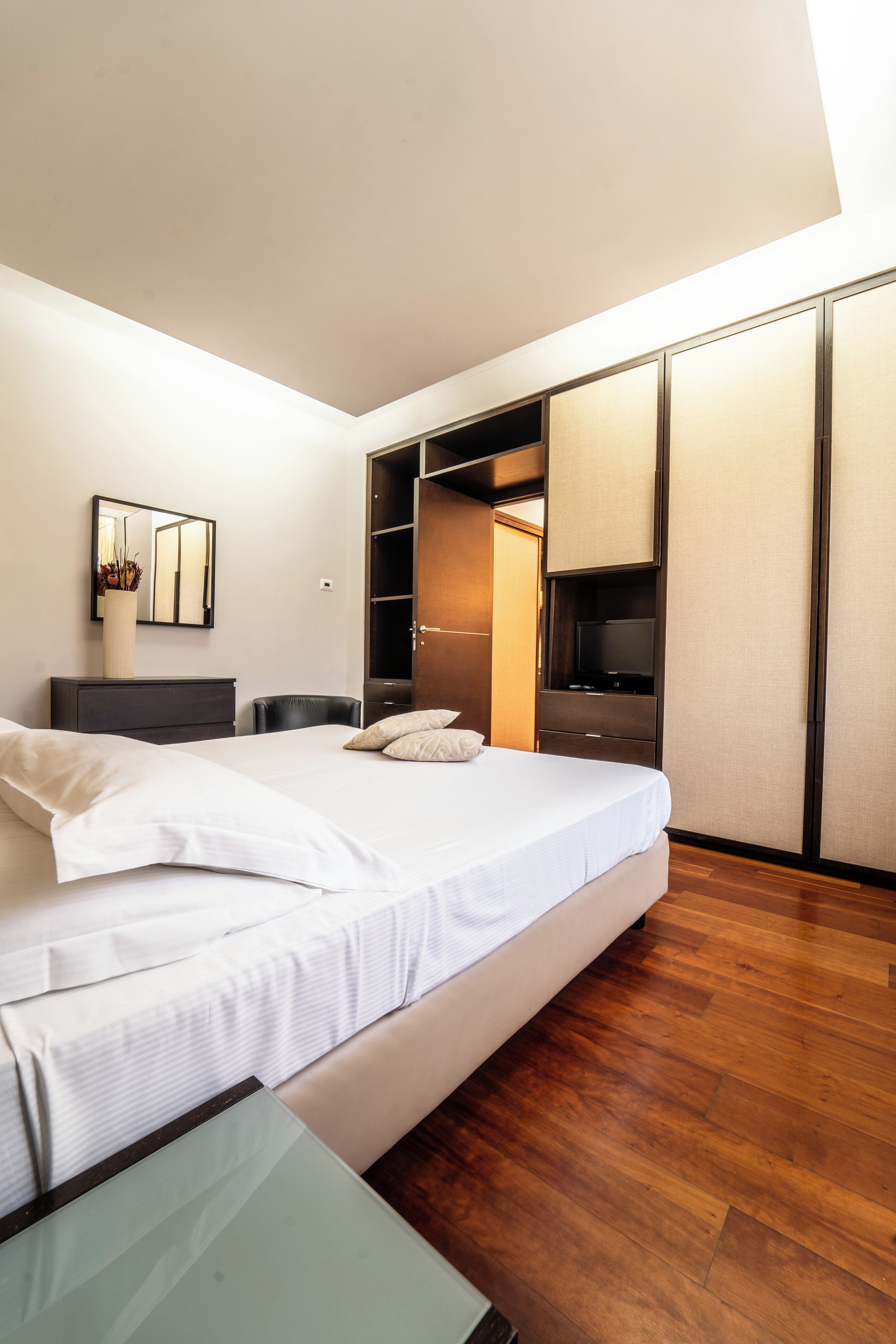 A modern bedroom with a large bed, a wardrobe, and a mirror.