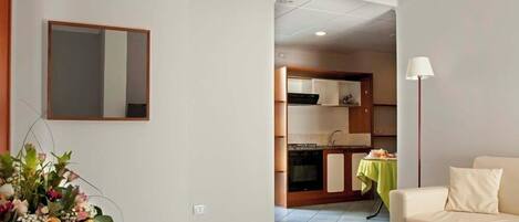 Una sala de estar con un sofá y una mesa verde, un área de cocina con armarios y una estufa, y un espejo en la pared.