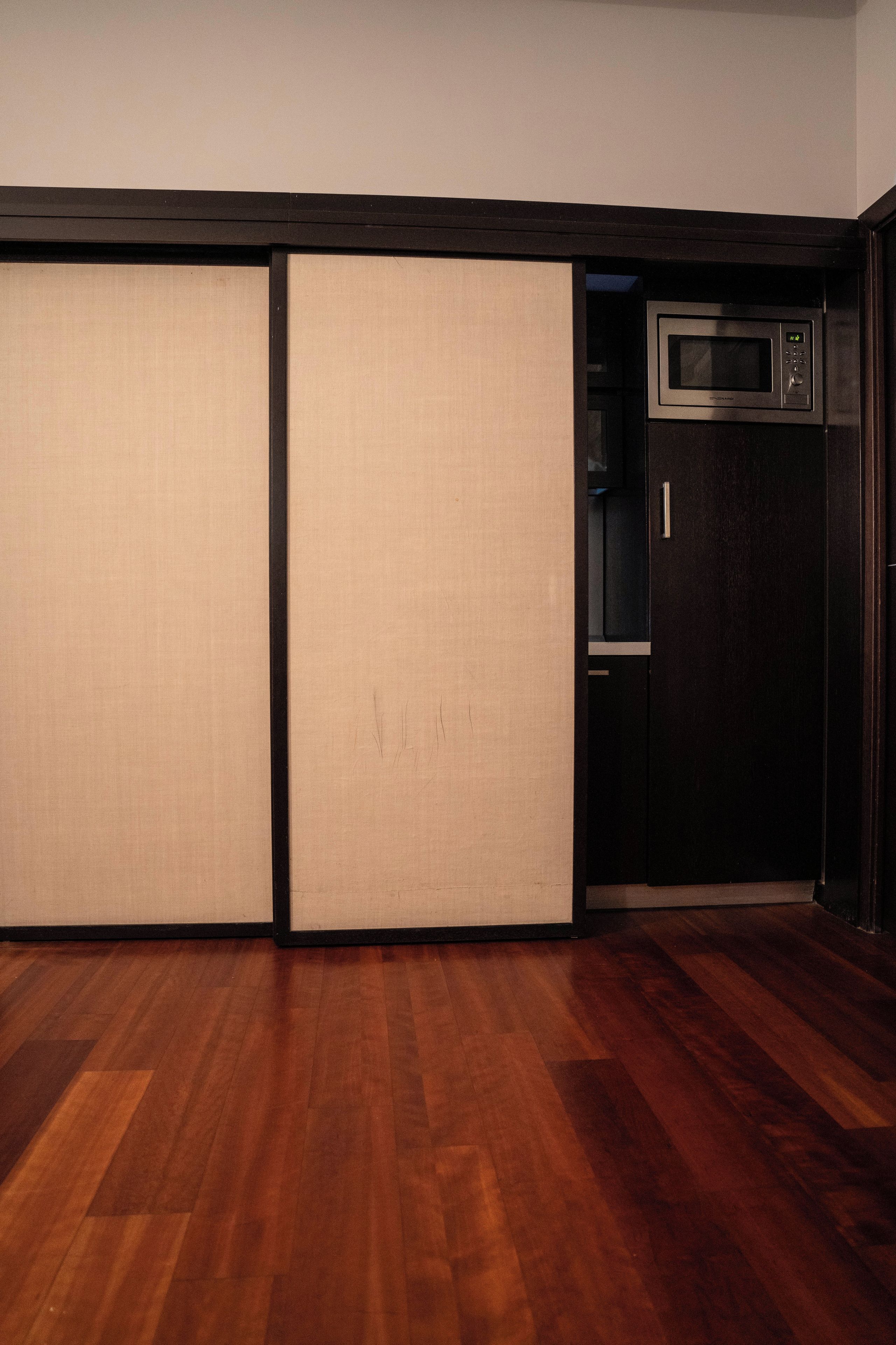 A room with a sliding door, a microwave, and a wooden floor.