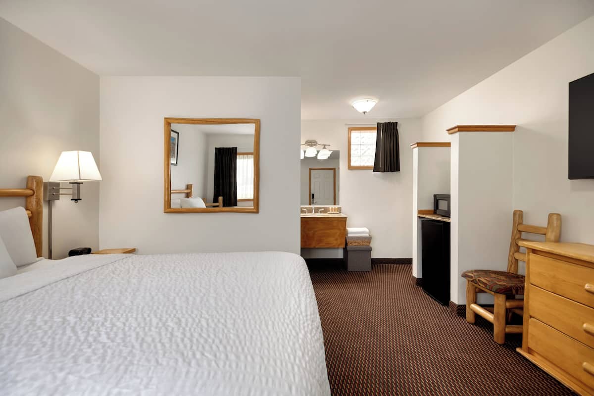A hotel room with a large bed, a desk with a computer, a chair, a dresser, a mirror, and a window with curtains.