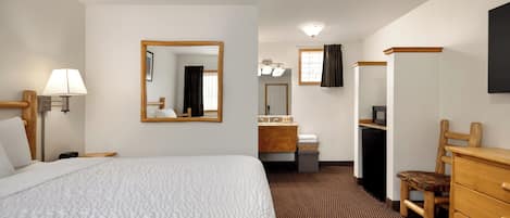 Ein Hotelzimmer mit einem großen Bett, einem Schreibtisch mit Computer, einem Stuhl, einer Kommode, einem Spiegel und einem Fenster mit Vorhängen.