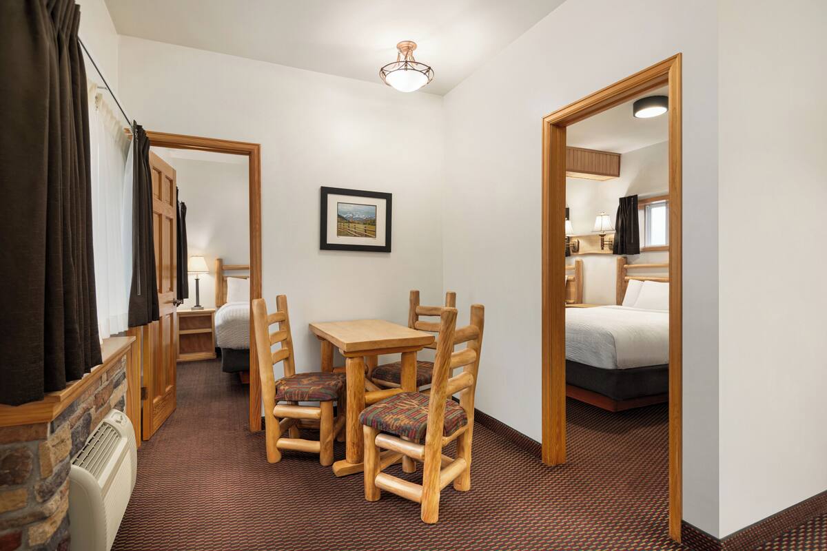 A compact hotel room with a bed, a small table with chairs, a framed picture on the wall, and a ceiling light fixture.