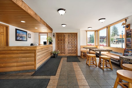 A reception area with a wooden reception desk, a black mat, wooden stools, and a view of the outside through large windows.. The Nordic Lodge