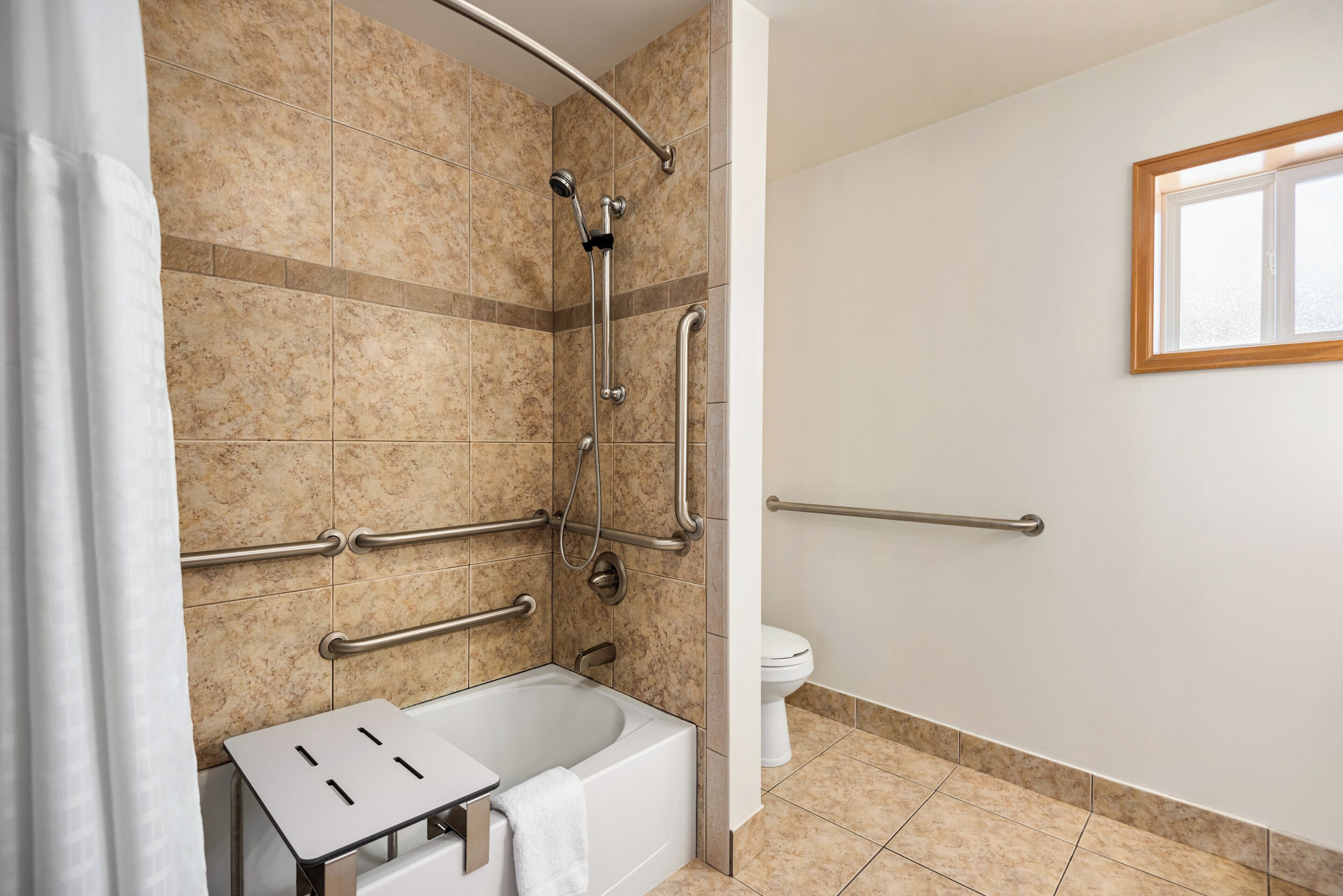 A bathroom with a shower, toilet, and a bathtub. It includes grab bars and a window.