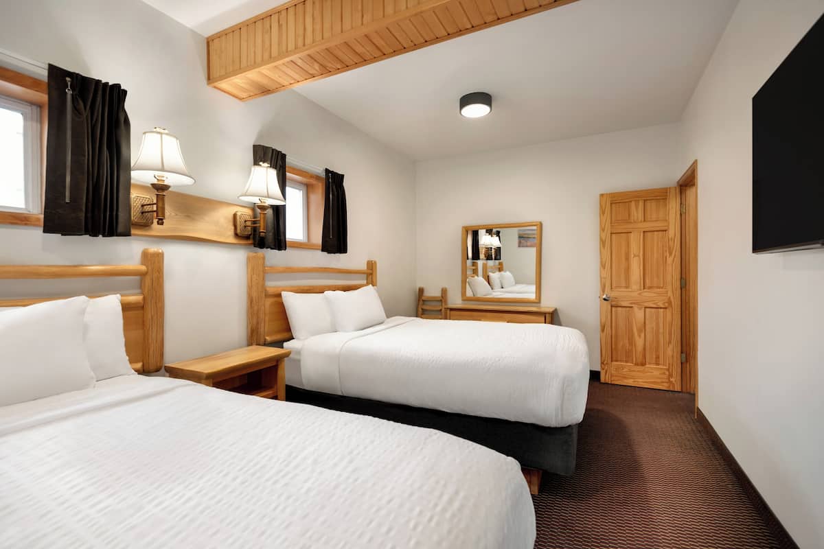 A hotel room with two beds, wooden headboards, bedside tables, lamps, a mirror, and a wooden door.