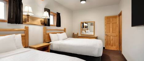 A hotel room with two beds, wooden headboards, bedside tables, lamps, a mirror, and a wooden door.