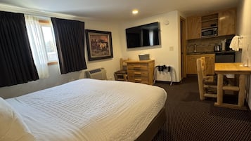 Camera d'albergo con un letto grande, una scrivania, una sedia, una televisione, un quadro, un forno a microonde e angolo cottura.