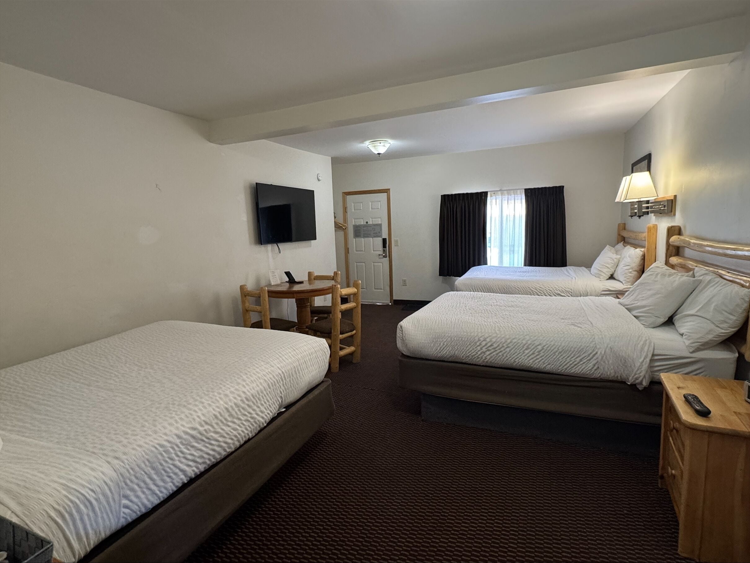 A hotel room with two beds, a desk, a TV, and a lamp.