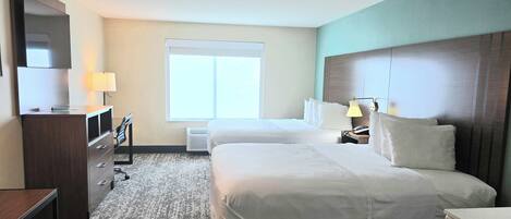 A hotel room with two beds, a desk, a TV, a lamp, and a window.