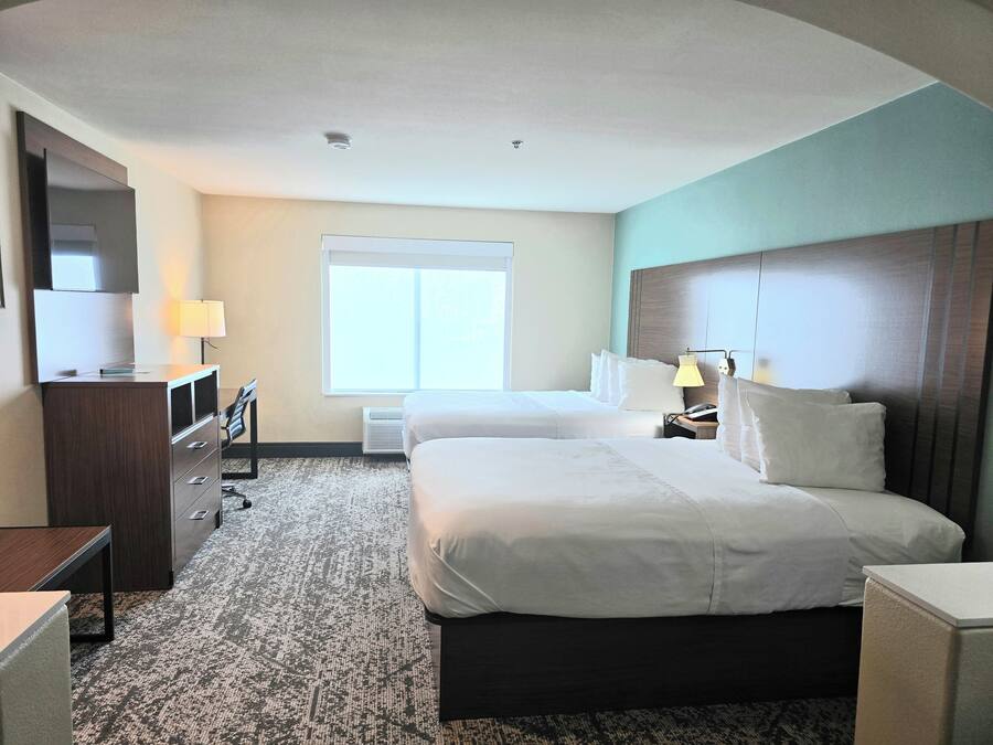 Habitación de hotel con dos camas, un escritorio, un televisor, una lámpara y una ventana.