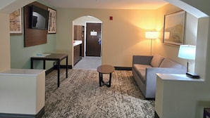 A hotel room with a sofa, a small table, a lamp, a TV, and a framed picture on the wall. - Best Western Casa Villa Suites (Harlingen)