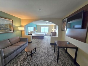 Une chambre d’hôtel avec un canapé, une petite table, un lit, un bureau et une télévision.