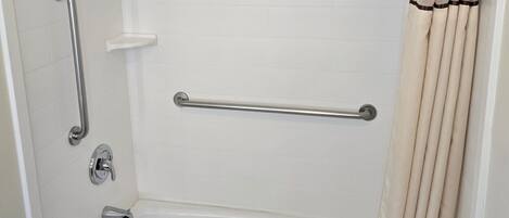 Une baignoire blanche standard, équipée d’un rideau de douche, de barres d’appui et d’un porte-serviettes.