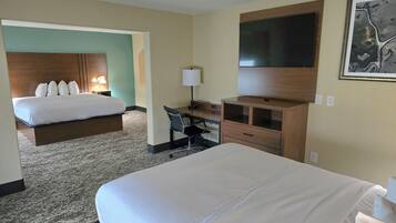 A hotel room with a large bed, a desk with a chair, a TV mounted on the wall, and a painting above the desk.