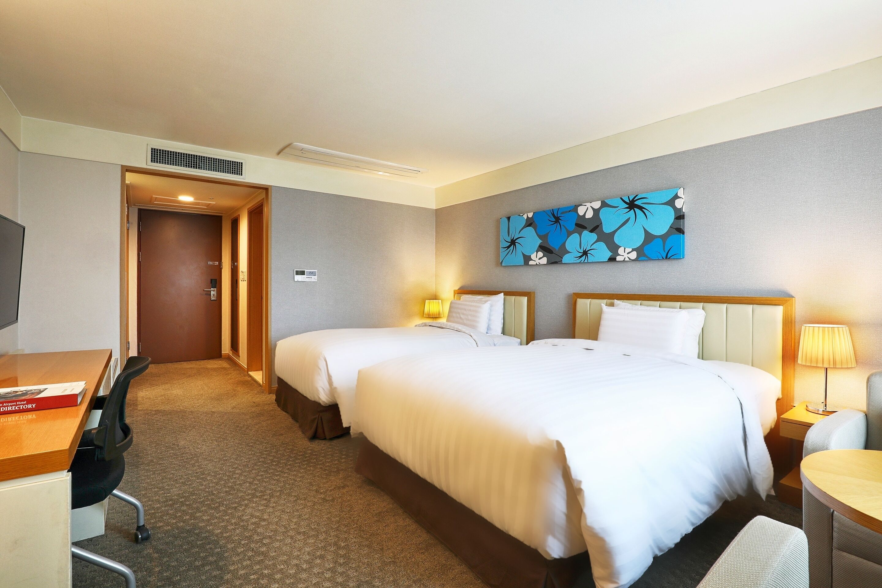 A hotel room with two beds, a desk with a chair, a TV, and a painting on the wall.