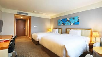 A hotel room with two beds, a desk with a chair, a TV, and a painting on the wall.