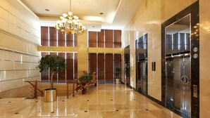 Eine geräumige Lobby mit poliertem Boden, einer beeindruckenden Kristallleuchtre und einem modernen Aufzug.