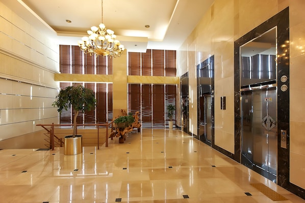 A spacious lobby with a polished floor, a grand chandelier, and a modern elevator.
