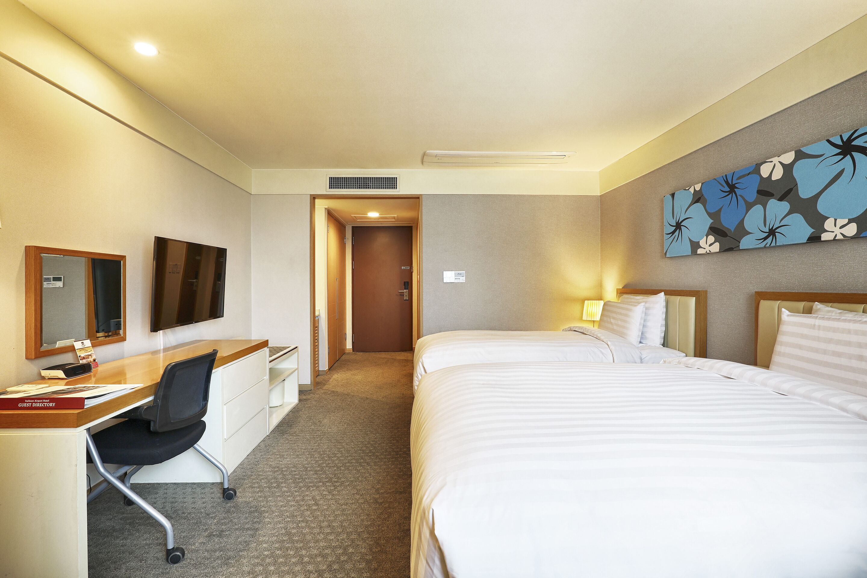 A hotel room with a bed, desk, chair, and a painting on the wall.