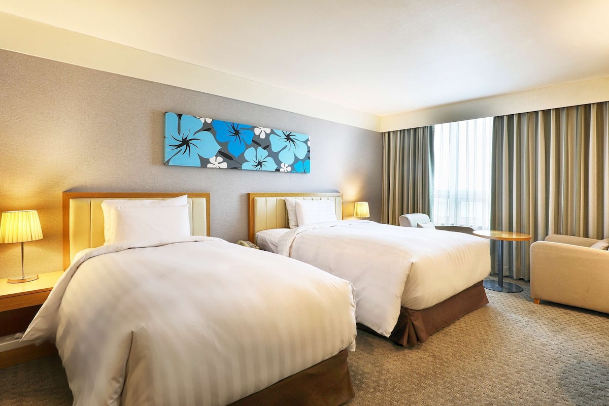 A hotel room with two beds, a sofa, a small table, and a painting on the wall.