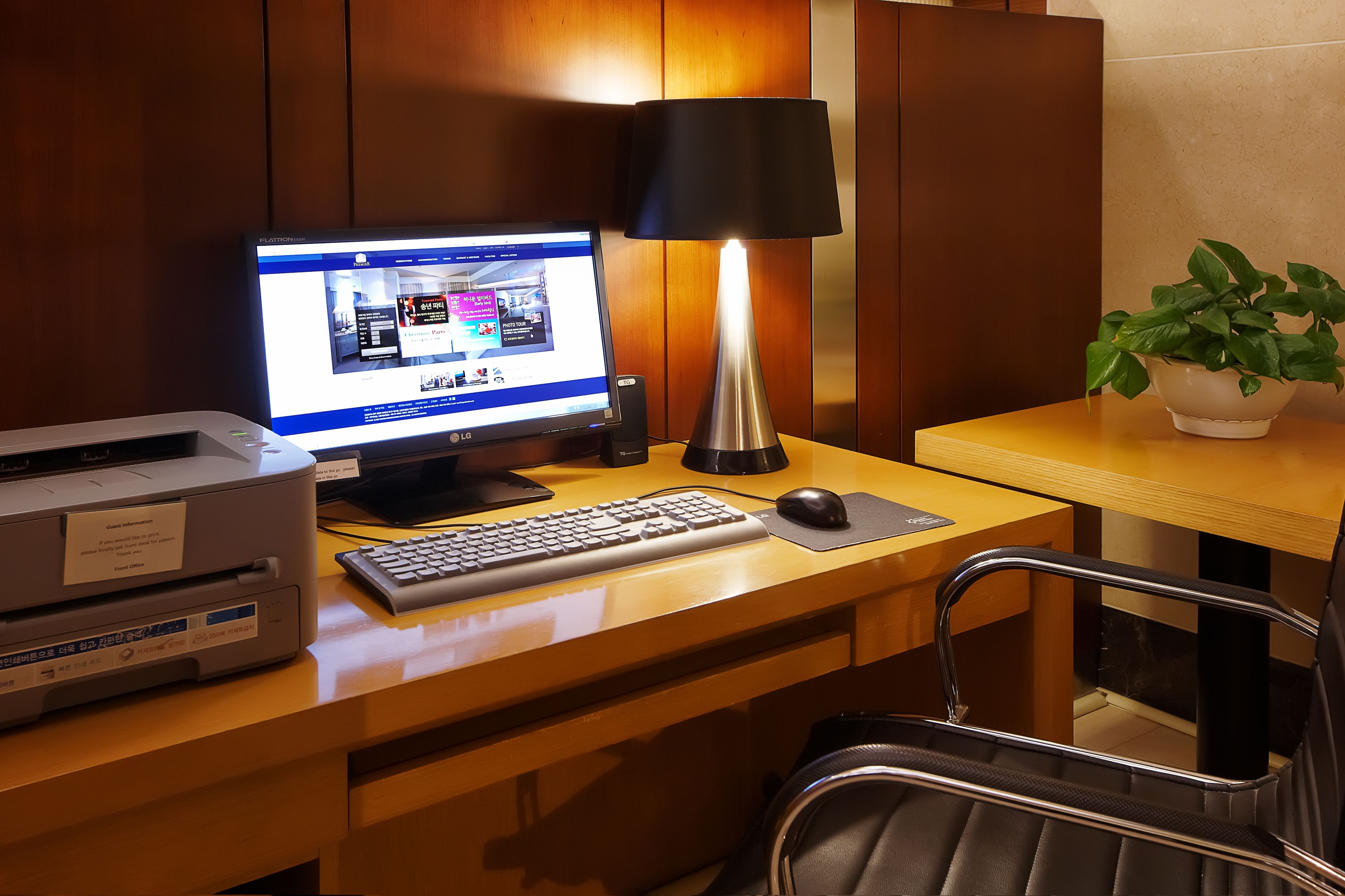 A hotel room desk with a computer, lamp, keyboard, mouse, and a printer.