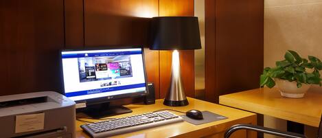 A hotel room desk with a computer, lamp, keyboard, mouse, and a printer.