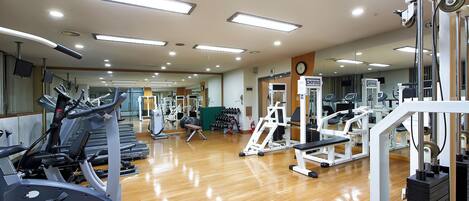 Un gimnasio con equipo de ejercicio, piso de madera y un reloj en la pared.