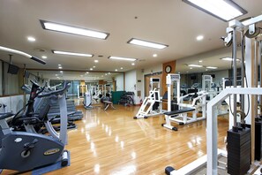 Une salle de sport équipée de matériel d’exercice, dotée d’un plancher en bois et d’une horloge au mur.