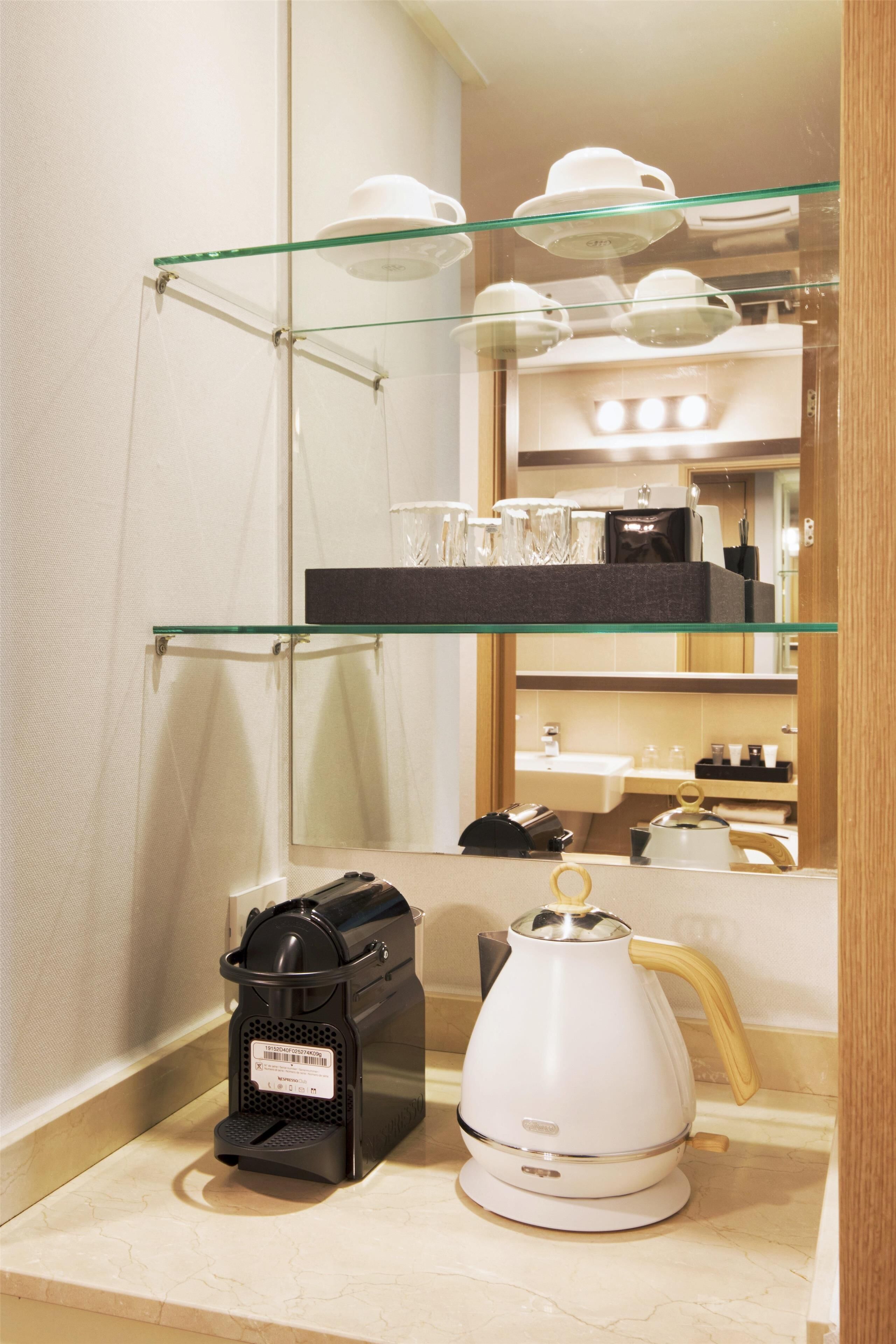 A bathroom with a coffee maker, a kettle, and a glass shelf with cups and a tea pot.
