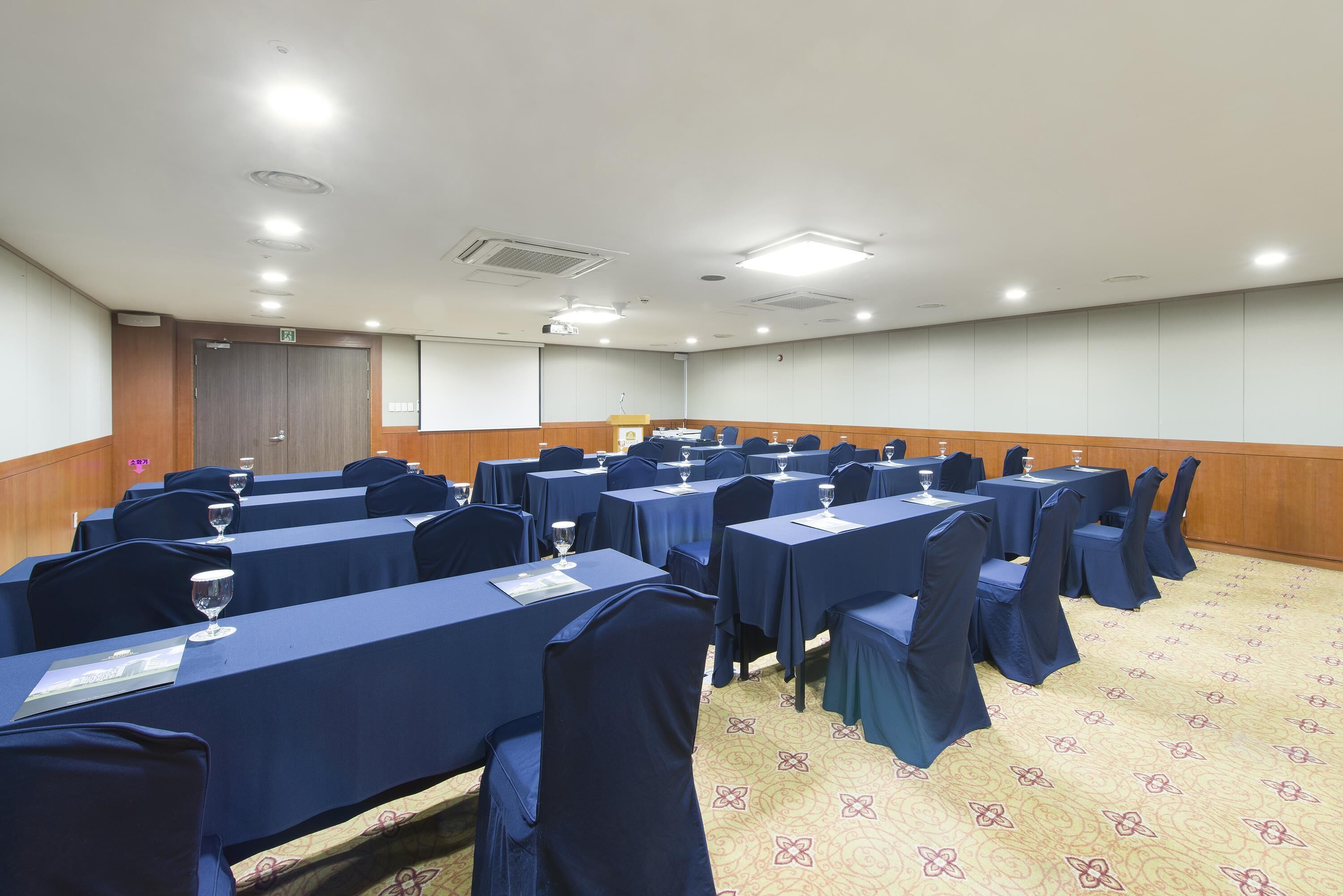 A conference room with rows of tables, chairs, and a podium.